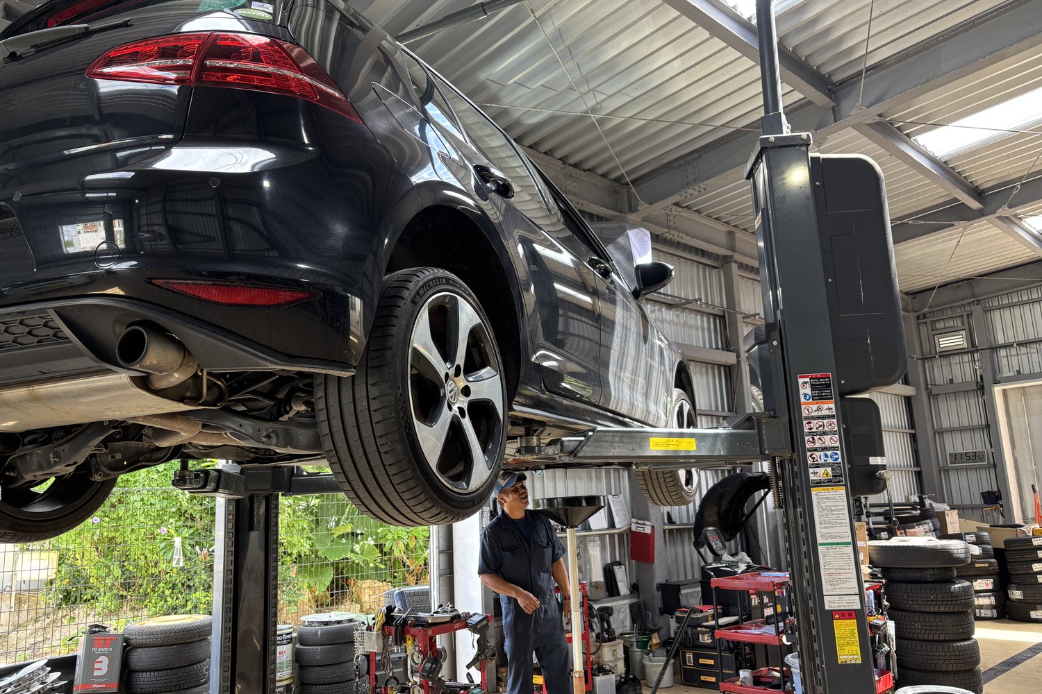 リフトで持ち上げられた車と、その奥で作業する整備士